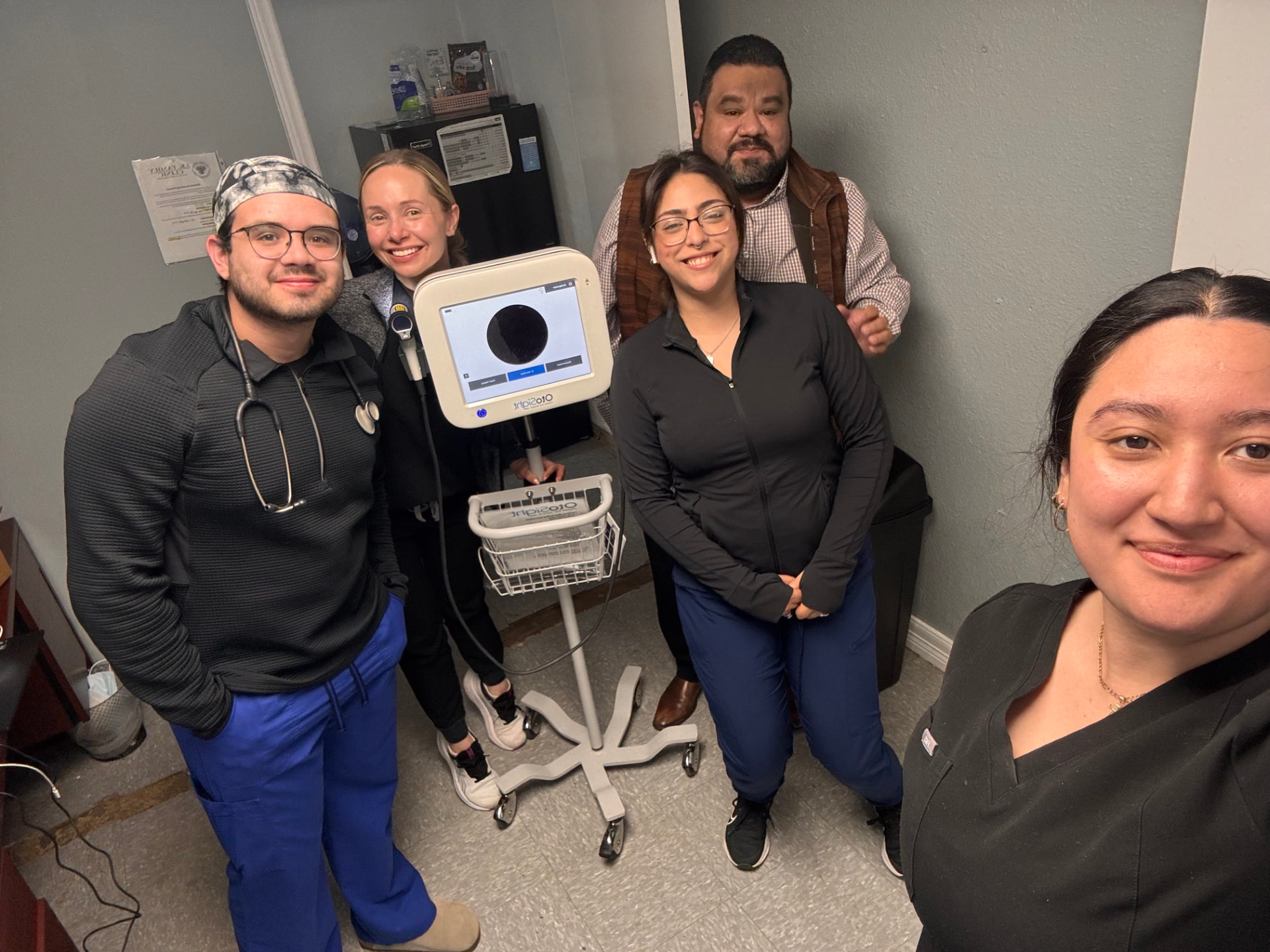 Clinic staff gathered around an OtoSight scope on a rolling stand