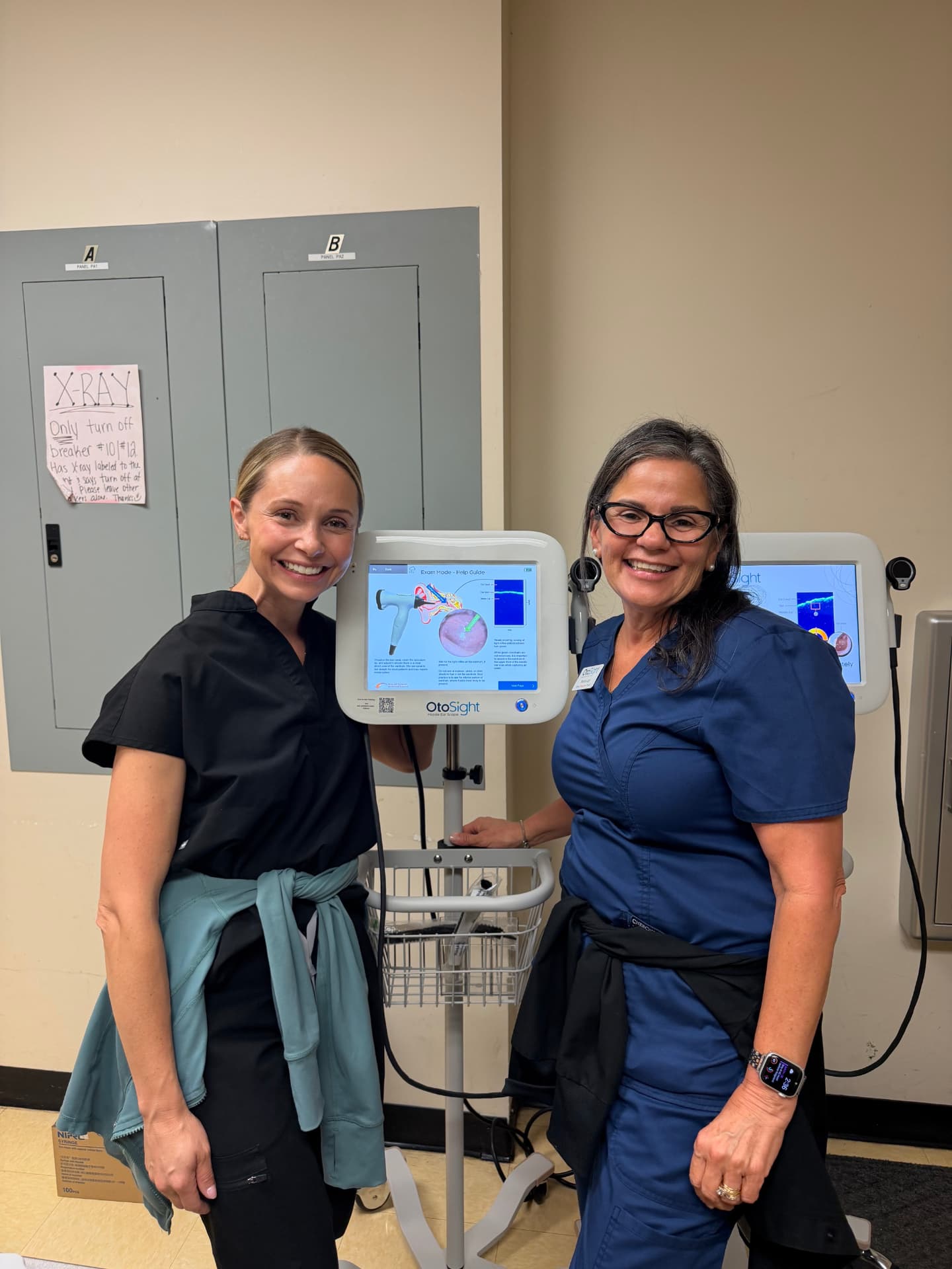 Two clinicians beside an OtoSight Middle Ear Scope cart in an exam room